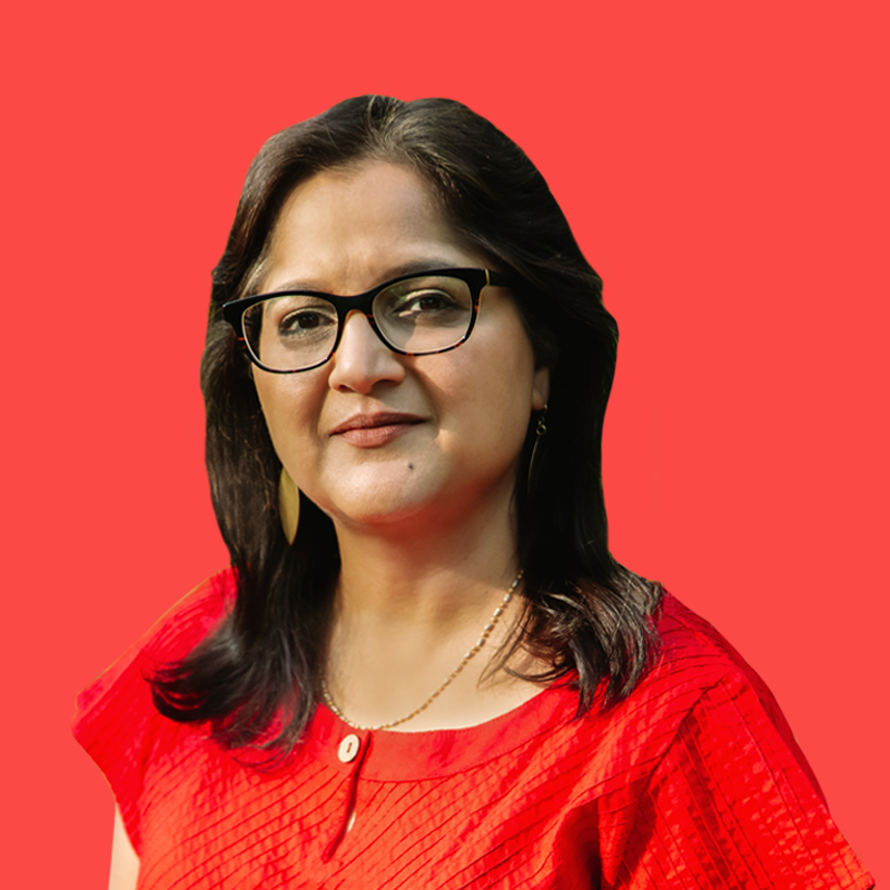 A person with long dark hair, wearing glasses and a red top, stands against a solid red background.