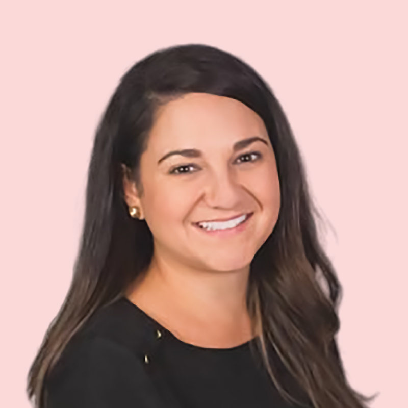 A person with long dark hair and a black top smiles against a light pink background.