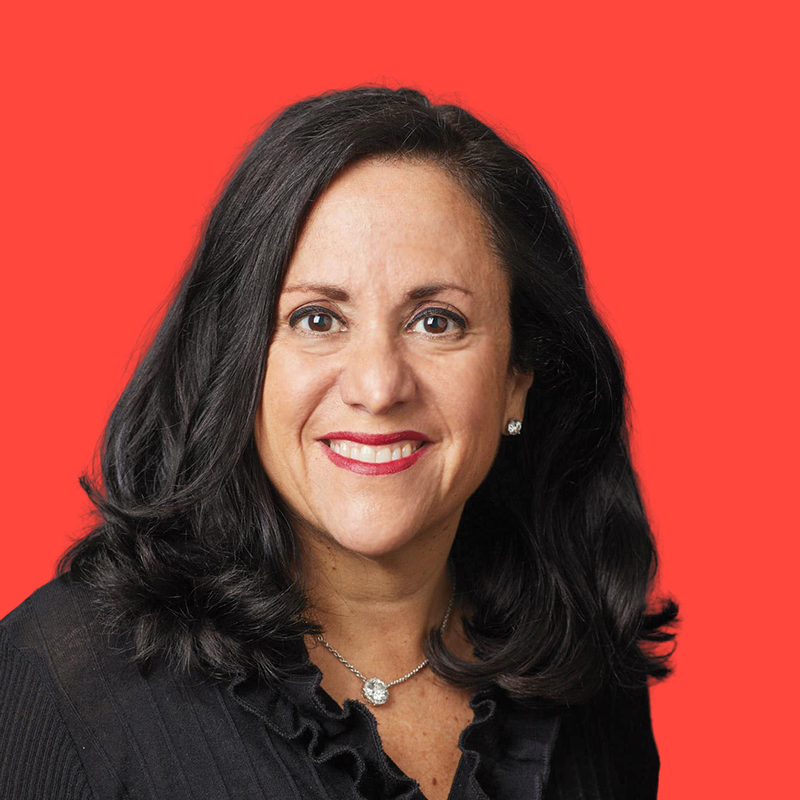 A woman with long dark hair wearing a black top and a necklace smiles against a solid red background.