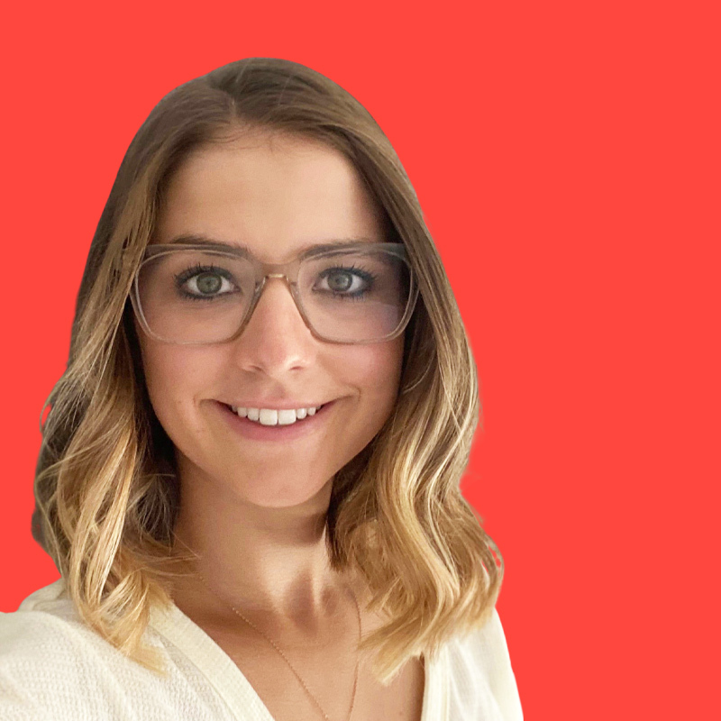 Person with shoulder-length hair and glasses smiling against a solid red background.