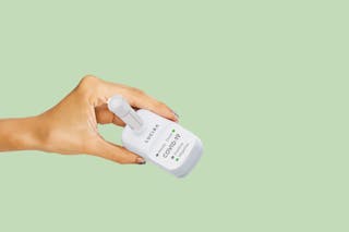 A hand holding a Lucira COVID-19 test device against a light green background.