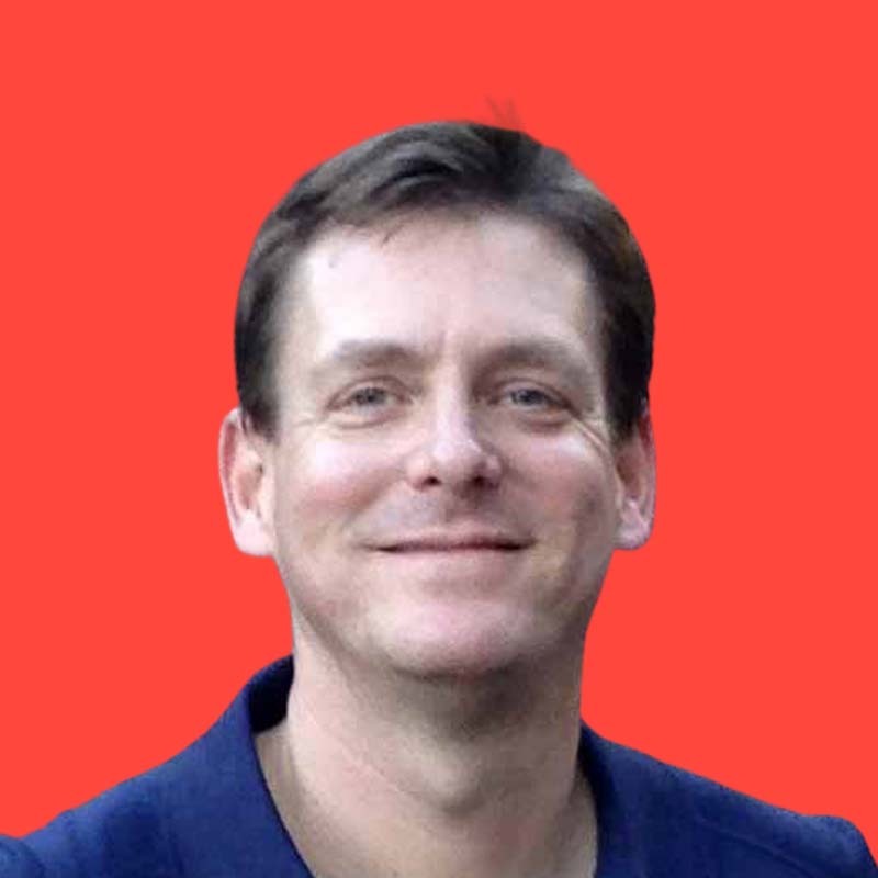 Smiling person with short brown hair against a red background.