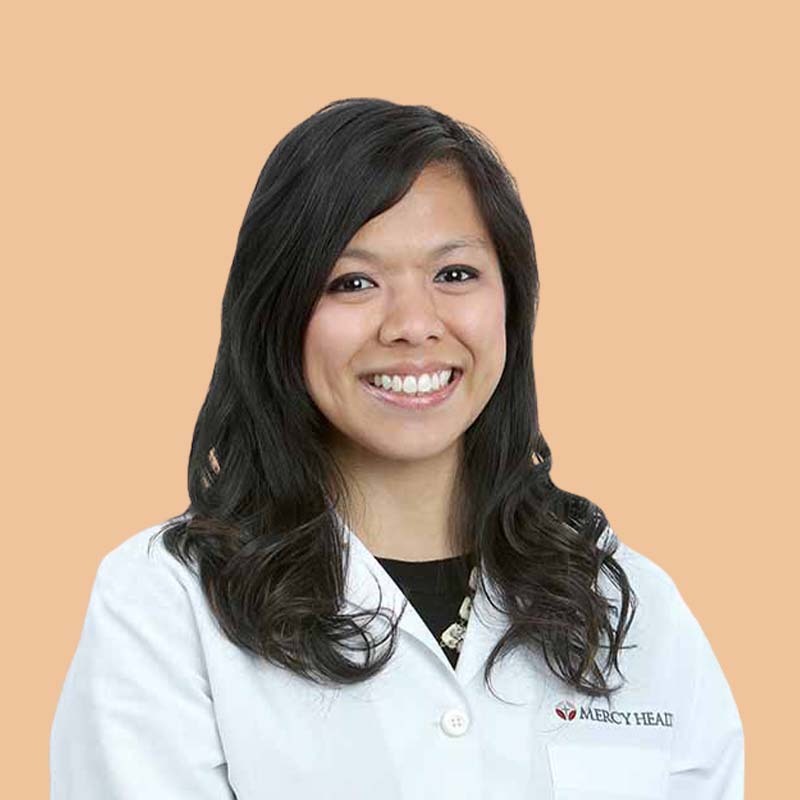 A person with long dark hair wearing a white lab coat smiles against a plain background.