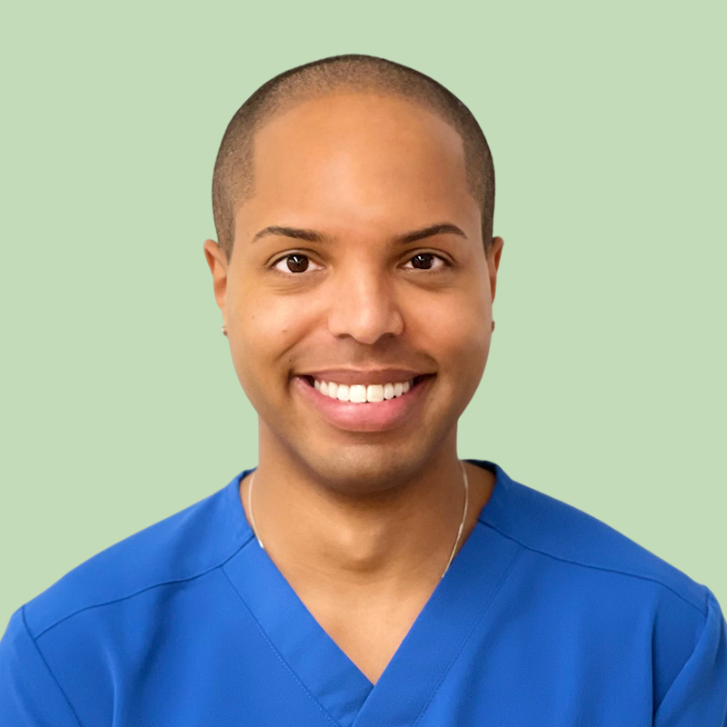 Person in blue scrubs smiling, posed against a light green background.