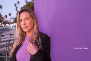 Woman with long blonde hair stands against a purple wall outdoors, wearing a lavender shirt and a black jacket. Text reads, 