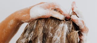 Primer plano de una persona lavándose el cabello, con las manos enjabonadas con jabón y champú.