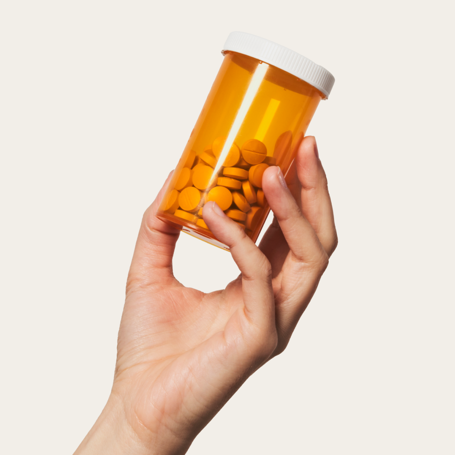 Hand holding a pill bottle filled with orange tablets, against a plain background.