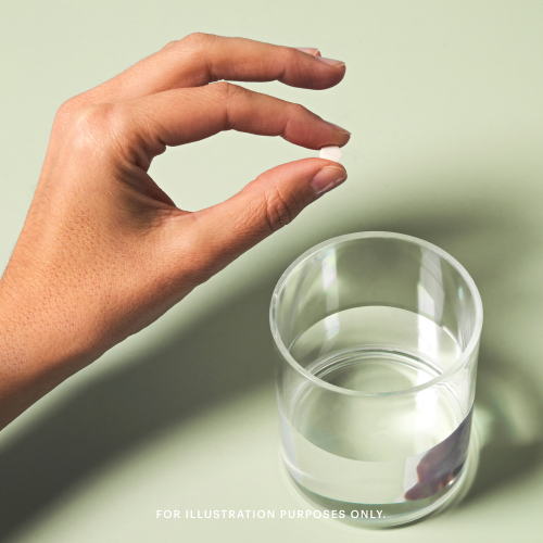 A hand holds a small pill above a clear glass of water on a light green surface. Text reads 