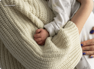 Baby wearing star-patterned onesie asleep in adult's arms with blue nail polish against a textured cream blanket.