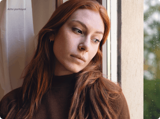 A person with long red hair gazes thoughtfully out of a window, wearing a dark sweater. The words 
