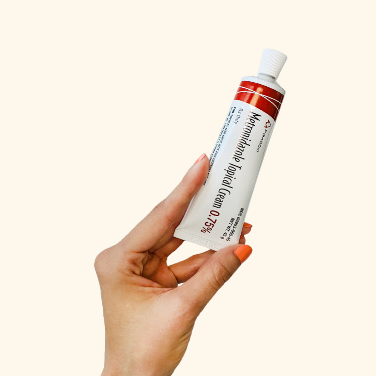 A hand holding a tube of Mometasone topical cream 0.1% with a red and white label.