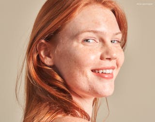 Person with long red hair and freckles smiling at the camera.