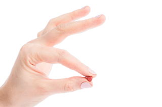 A hand holding a small brown pill between the thumb and index finger against a white background.