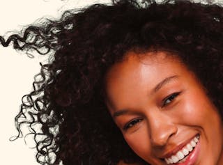 Close-up of a person with curly hair smiling broadly against a plain background.