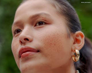 Close-up of a person with freckles, wearing gold hoop earrings, looking upward. Text in the image reads 