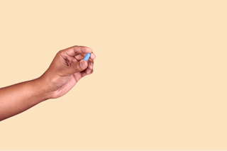 A hand holding a small blue chalk against a plain beige background.
