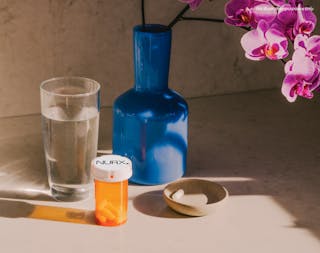 A glass of water, a blue vase with pink orchids, a pill bottle labeled 