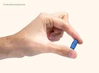 A hand holds a small, blue pill between the thumb and index finger against a neutral background.