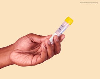 A hand holding a test tube with a yellow cap against a beige background. The test tube contains a small amount of clear liquid. Text reads, 