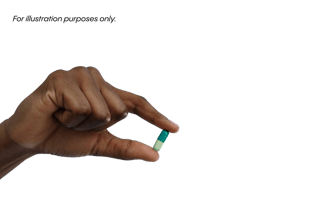 A hand holding a small green and white capsule between thumb and forefinger against a black background.