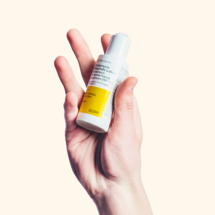 A hand holds a small white bottle with a yellow label against a plain background.