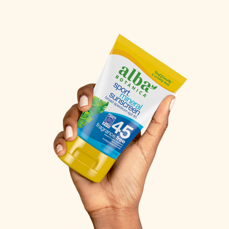 A hand holding Alba Botanica Sport Mineral Sunscreen SPF 45 tube against a plain background.