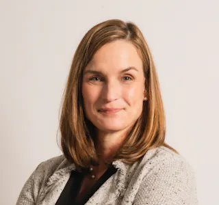 Woman with shoulder-length hair, wearing a blazer, smiling at the camera against a plain background.