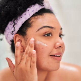 Person applying tretinoin cream with a purple headband, looking to the side.