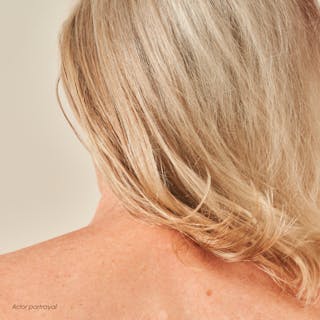 A person's back with shoulder-length blonde hair, glowing subtly as if nurtured by Tretinoin Cream, stands against a plain background.