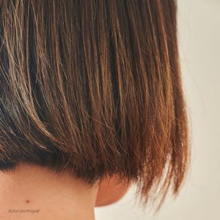 Close-up of a person's short brown hair styled in a bob cut, radiating health and shine as if complemented by the nourishing effects of Tretinoin Cream. The background is a soft, neutral color.