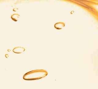 A close-up of golden oil droplets, reminiscent of the rich texture of tretinoin cream, suspended in a pale liquid background.
