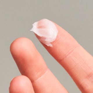 A close-up of a hand with a small amount of Tretinoin Cream on the tip of one finger against a light background.