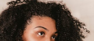 Close-up of a person with curly black hair and brown eyes, gazing upwards.