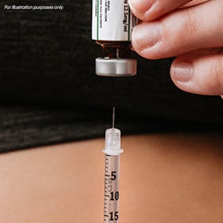 A person holds a vial and fills a syringe with liquid medication.