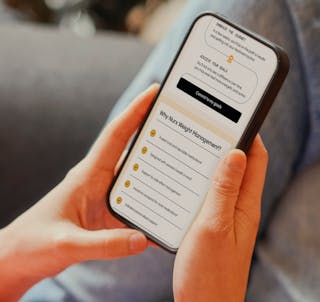 A person is holding a smartphone displaying a webpage about weight management, with a list of benefits and a 