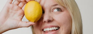 Person holding a lemon up to their left eye, smiling.