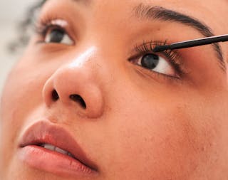 A person applies mascara to their upper eyelashes, focusing intently.